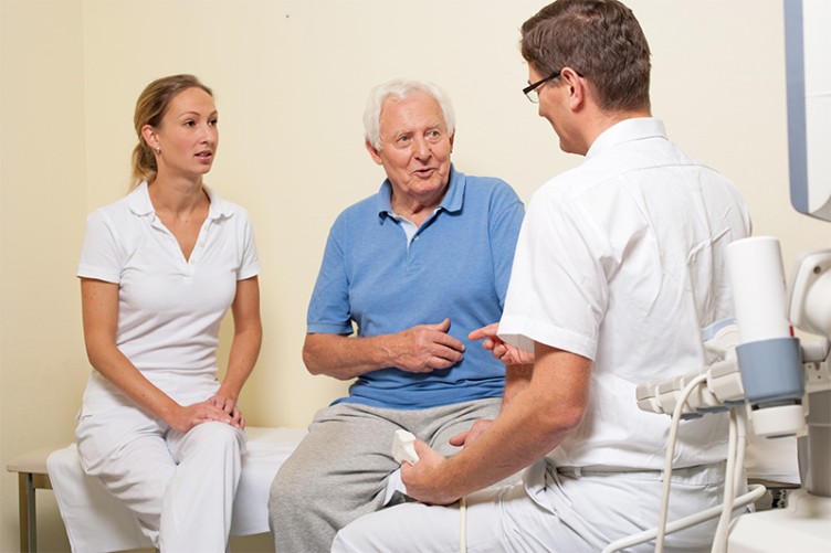 Ein älterer Patient spricht mit einem Arzt und einer Pflegerin im Krankenhaus