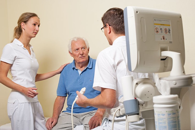 Ein Arzt und eine Ärztein im Gespräch mit einem Patienten vor einer Ultraschalluntersuchung