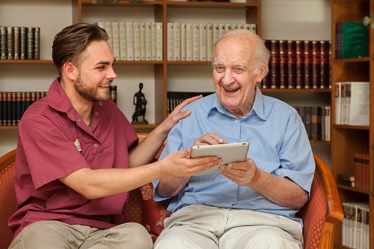 Ein Pfleger und ein pflegebedürftiger Mann arbeiten mit einem Tablet