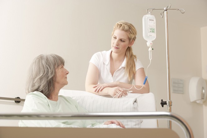 Eine Pflegerin steht am Krankenhausbett einer Patientin