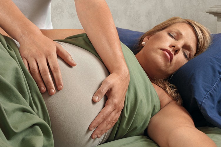 Eine Hebamme tastet den Bauch einer Schwangeren ab