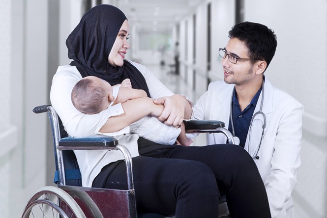 Eine Frau im Rollstuhl mit Baby im Arm und ein Arzt unterhalten sich im Krankenhaus