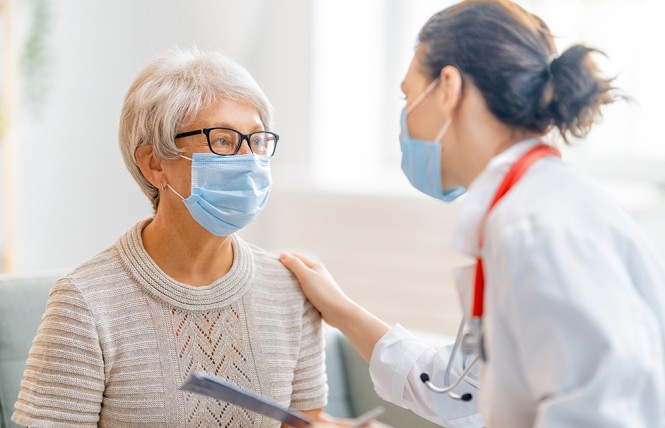 ältere Frau mit Mundschutz sitzt vor Ärztin