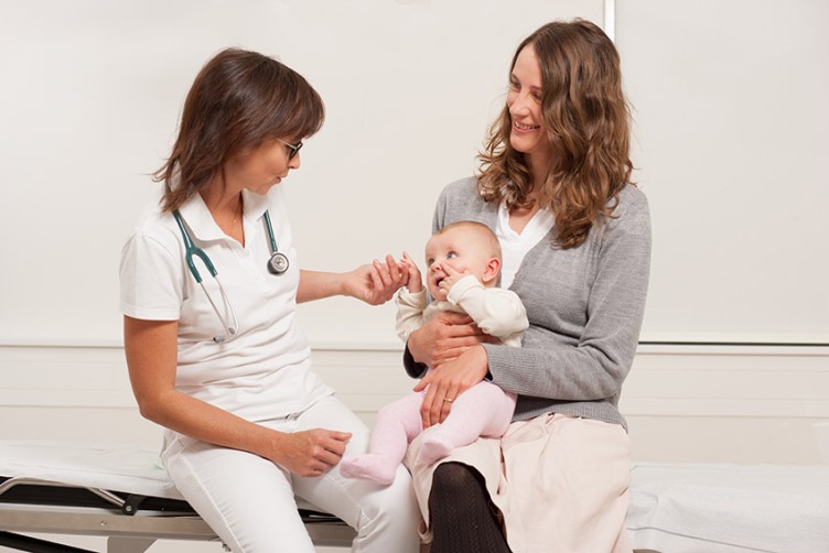 Eine Ärztin untersucht ein Baby auf dem Schoß seiner Mutter