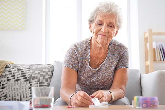 Eine ältere Frau nimmt sich ein Medikament, das vor ihr auf dem Tisch liegt.