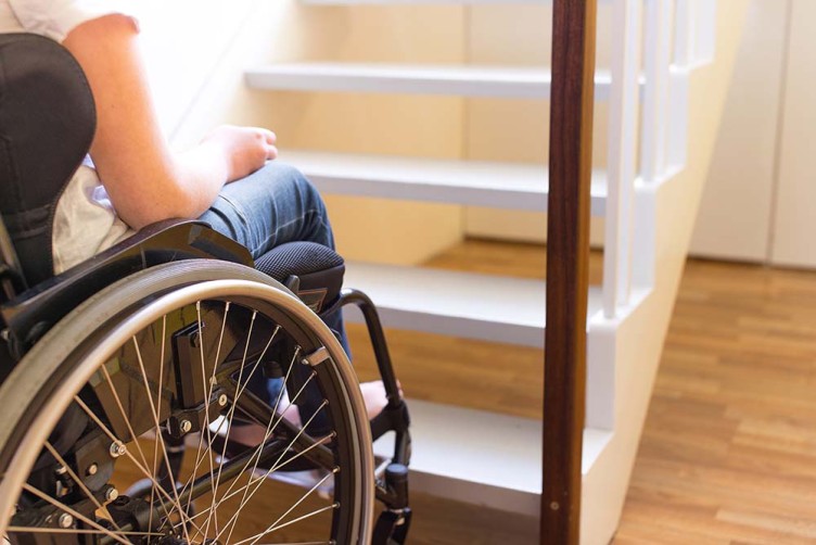 Eine Rollstuhlfahrerin steht vor einer Treppe, die eine Barriere darstellt.