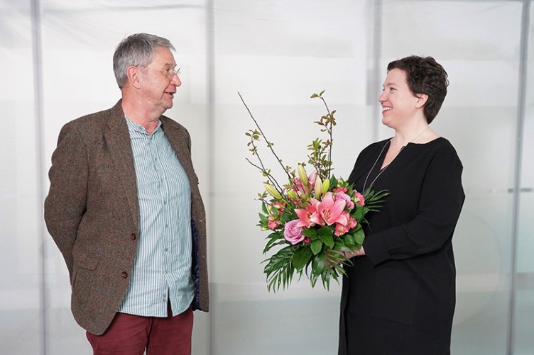 Herr Klemens spricht mit Frau Wagenmann, die einen Blumenstrauß hält