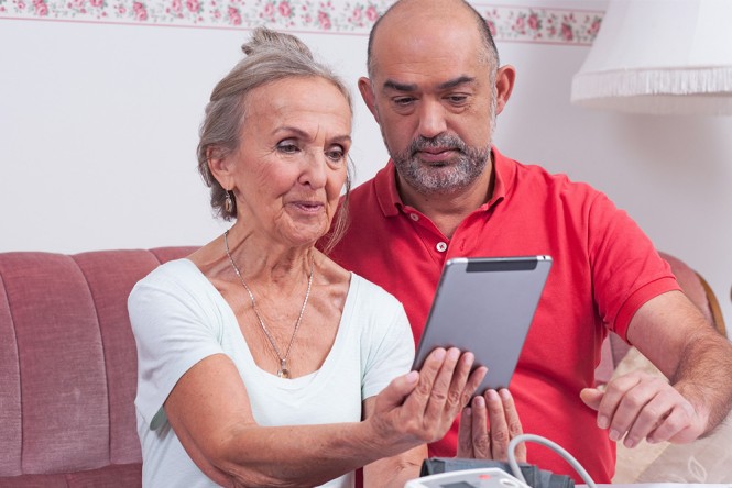 Eine ältere Frau und ein Pfleger schauen auf ein Tablet