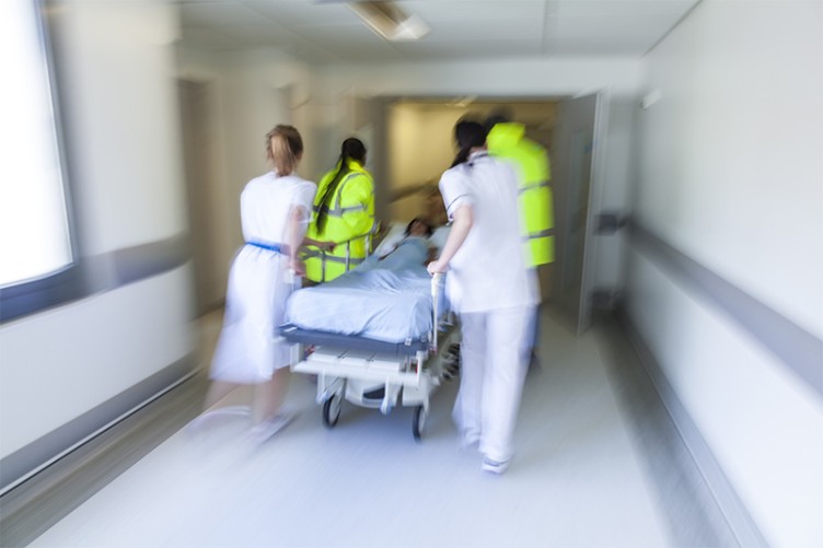 Ärzte und Pfleger schieben einen Patienten im Bett in großer Eile durch einen Krankenhausflur.