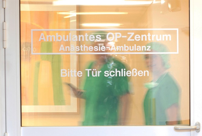 Hinter einer Tür zum Zentrum für Ambulantes Operieren stehen zwei Pflegekräfte
