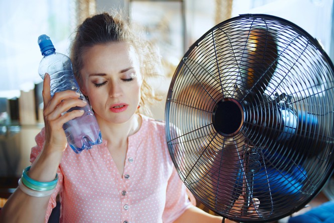 Eine Frau vor einem Ventilator kühlt sich die Stirn mit eine Wasserflasche